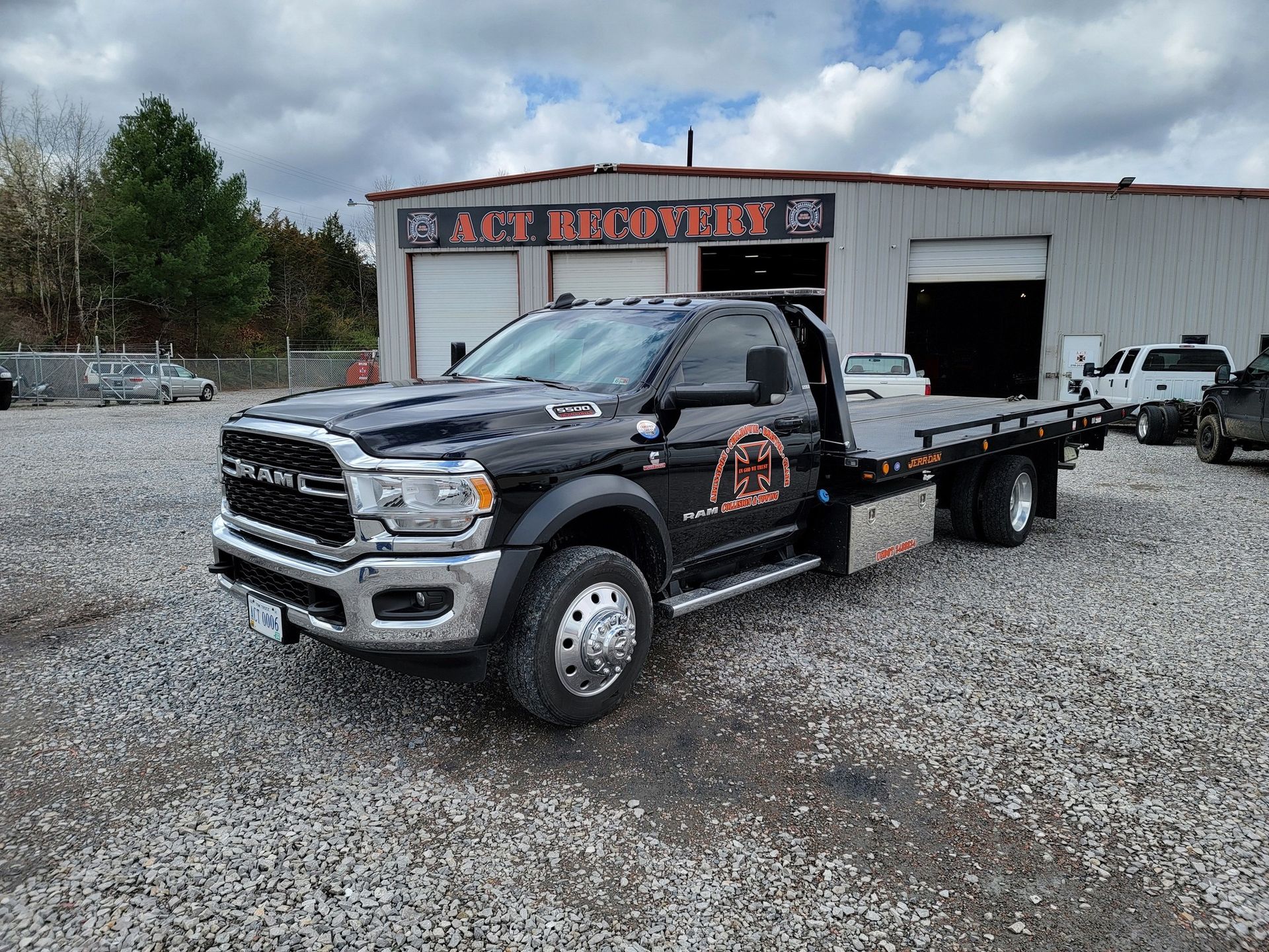 Black tow truck parked in front of a repair shop with the name 