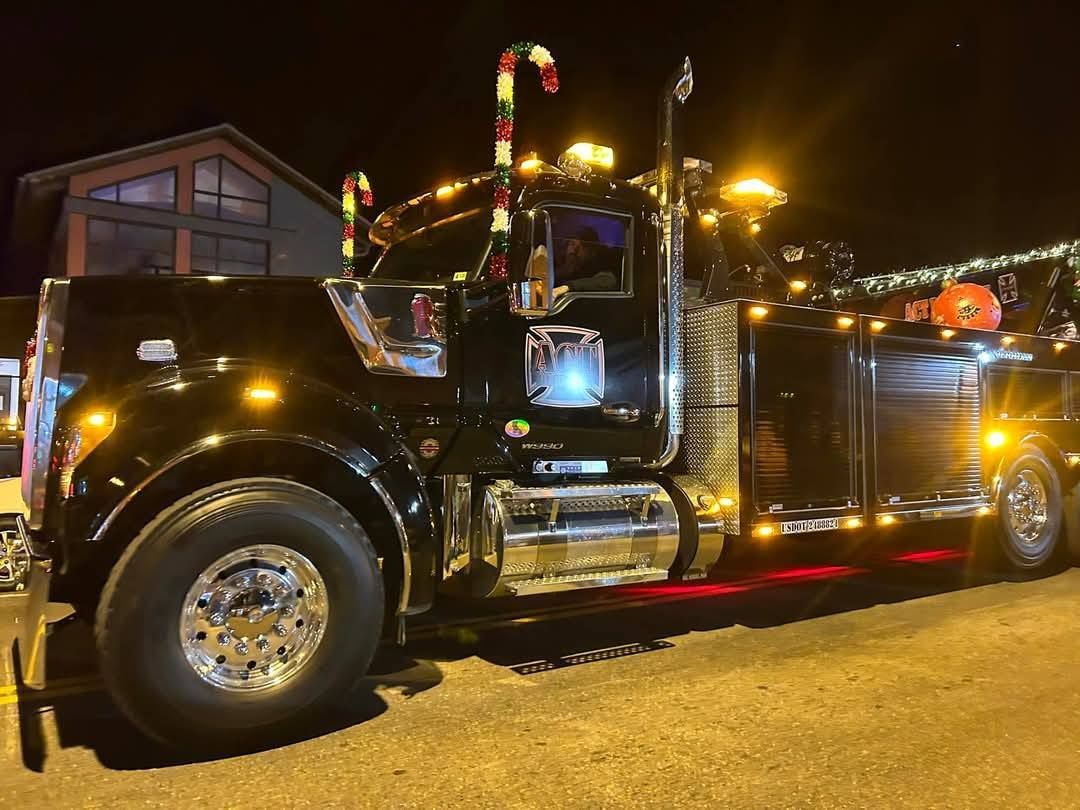 Black tow truck decorated with Christmas lights and candy canes at night.