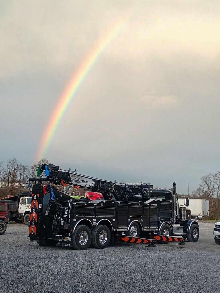 Tow truck under a rainbow, parked on gravel.