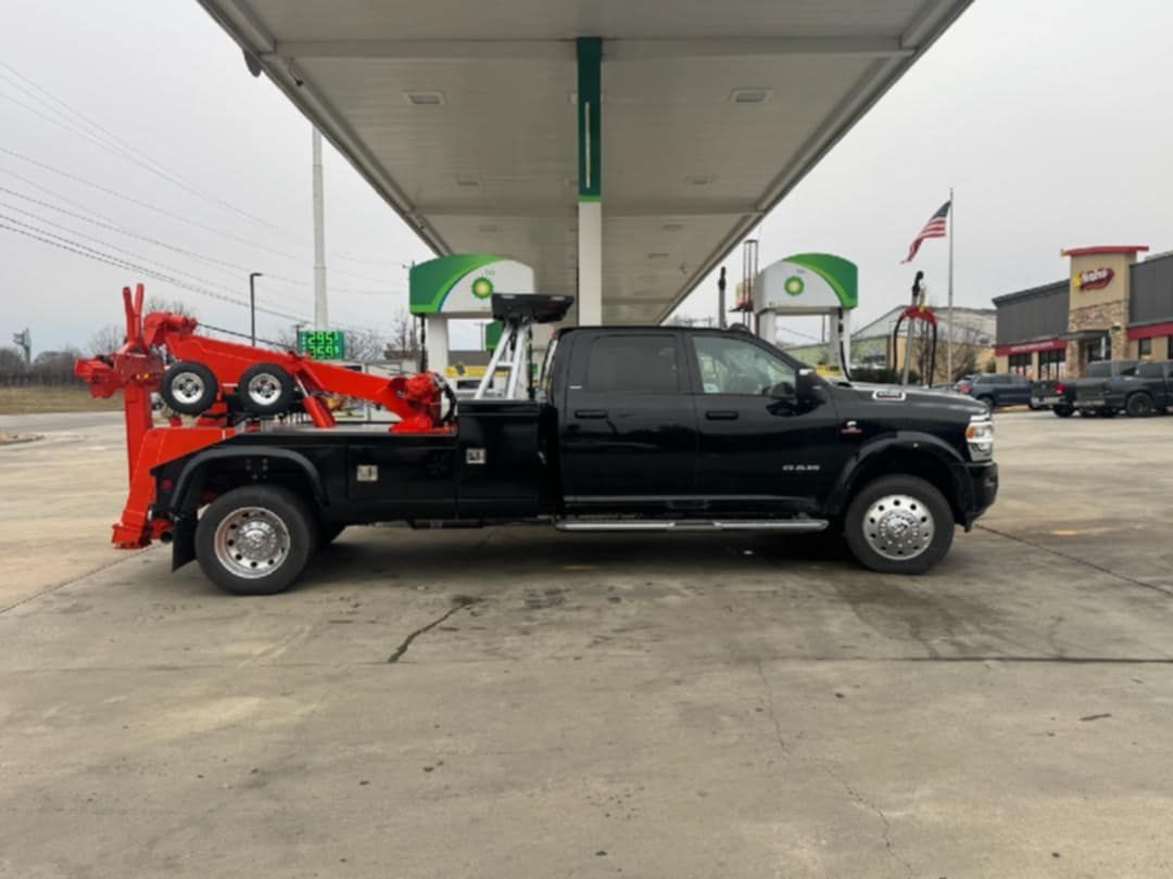 Black tow truck with orange towing equipment parked at a gas station.