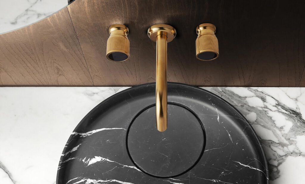 Lavabo rotondo nero con rubinetto dorato e due manopole, su un piano in marmo.