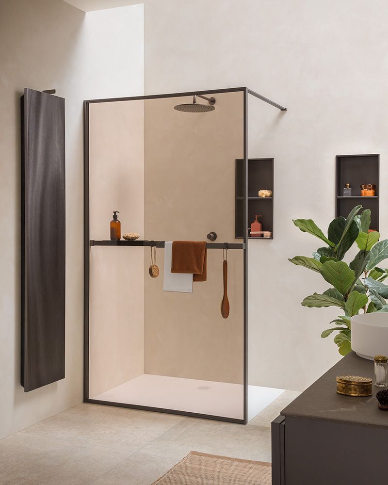 Bagno moderno con box doccia in vetro, pareti beige, sanitari scuri, portasciugamani e pianta in vaso sul mobiletto del lavabo.