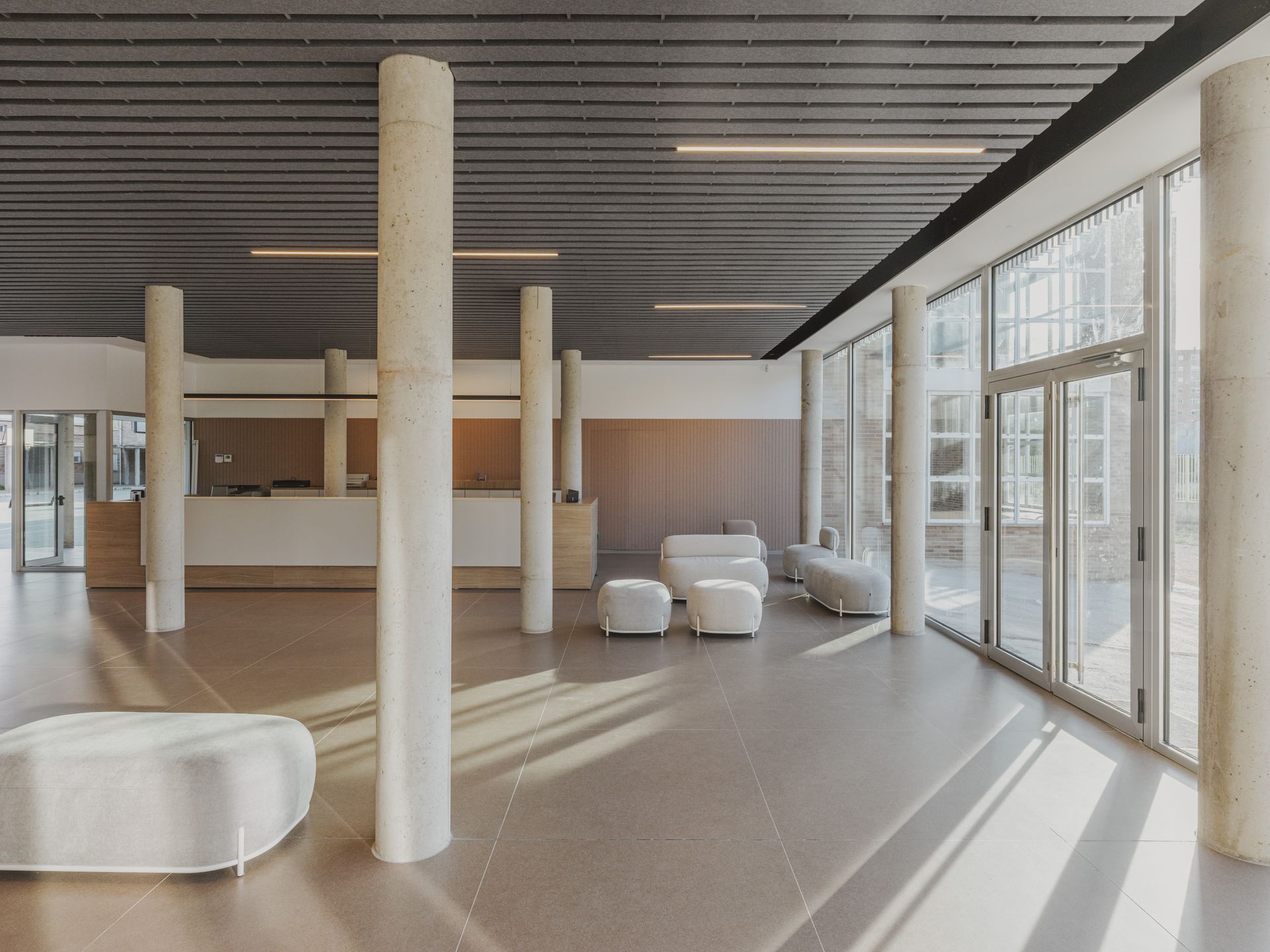 Luminosa e moderna hall con poltrone bianche, alte colonne e pareti di vetro illuminate dalla luce del sole.