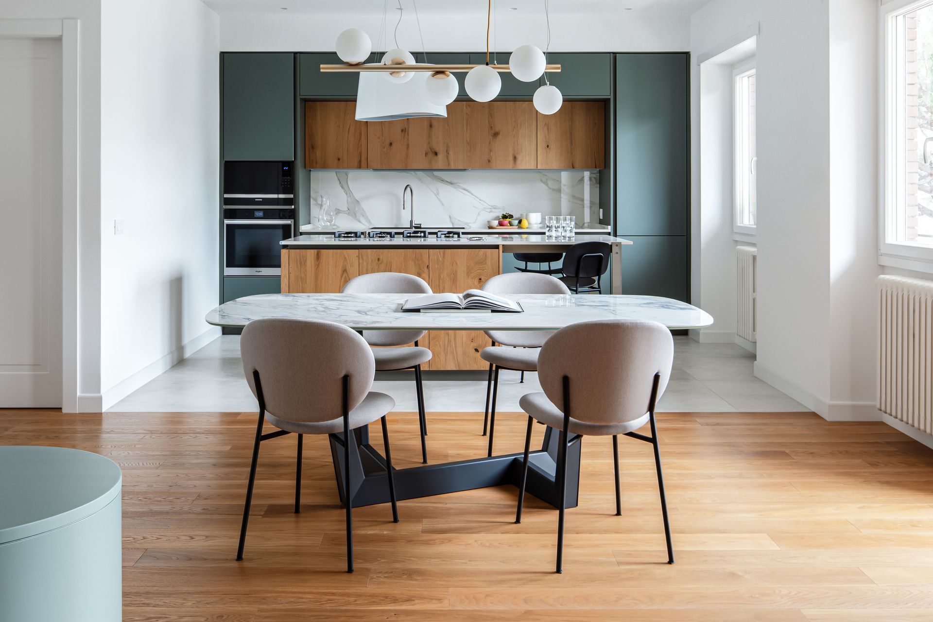 Sala da pranzo moderna con tavolo rotondo, sedie beige e cucina a vista con dettagli in legno.