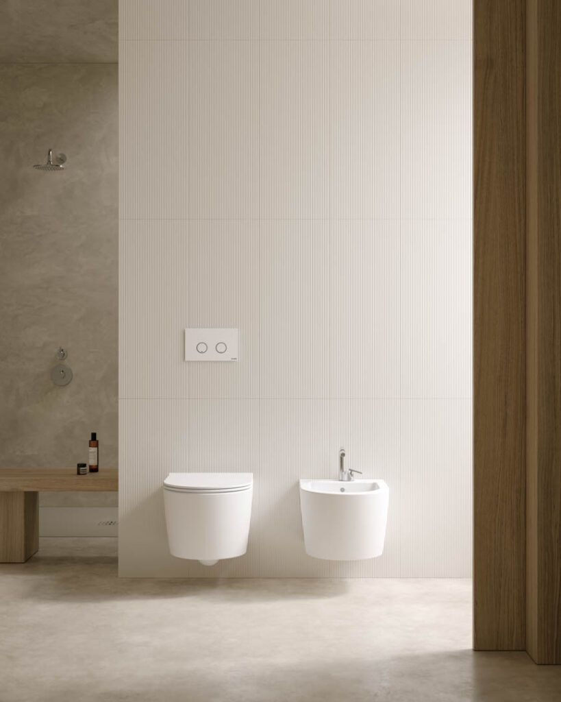 Bagno moderno con due WC sospesi bianchi, piastrelle beige e dettagli in legno.