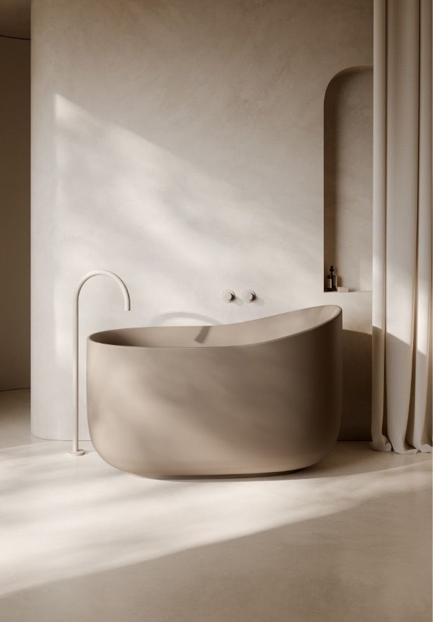 Bagno minimalista sui toni del beige con vasca da bagno rotonda freestanding, immerso in una luce solare soffusa.