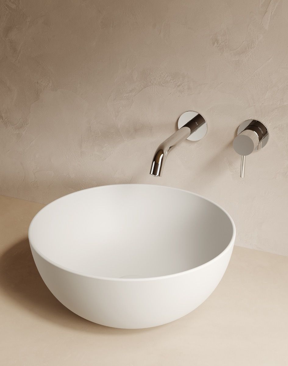 Lavabo da appoggio bianco con rubinetto a parete cromato, su una parete piastrellata beige.