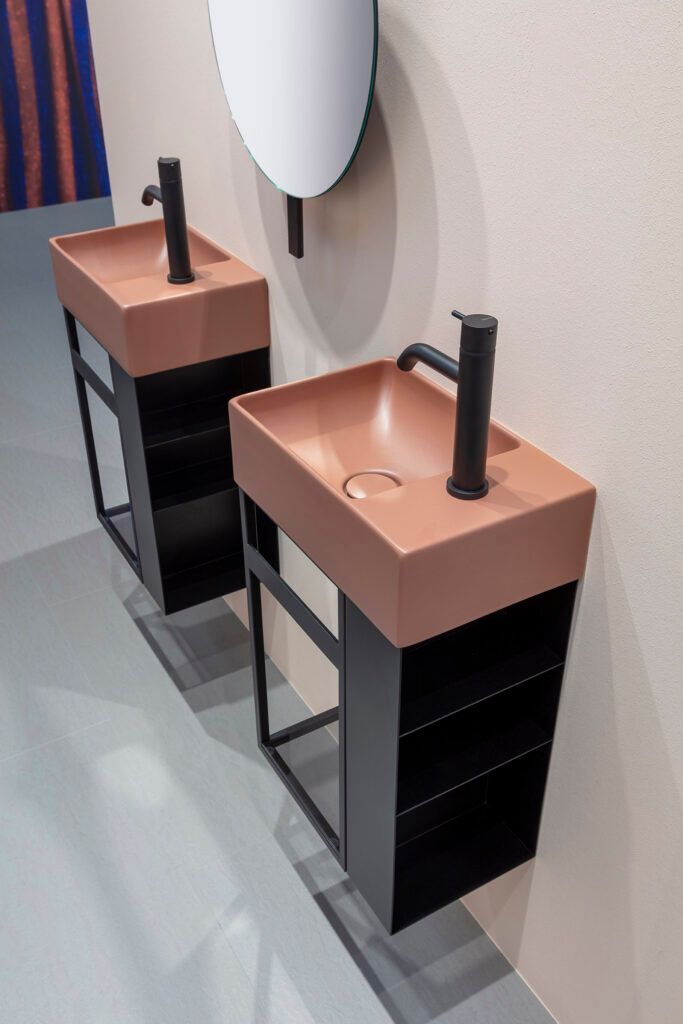 In un bagno, due moderni lavabi a colonna con mobili laterali neri, visti accanto a uno specchio a parete.