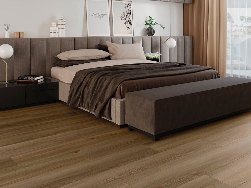 Camera da letto moderna con letto grande, testiera beige, biancheria da letto scura e pavimento in legno.