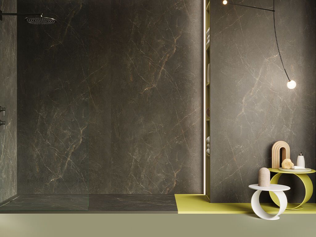 Interno moderno con pareti scure dalla texture particolare, finiture dorate e un piccolo tavolo rotondo bianco e giallo sotto una lampada a sospensione.