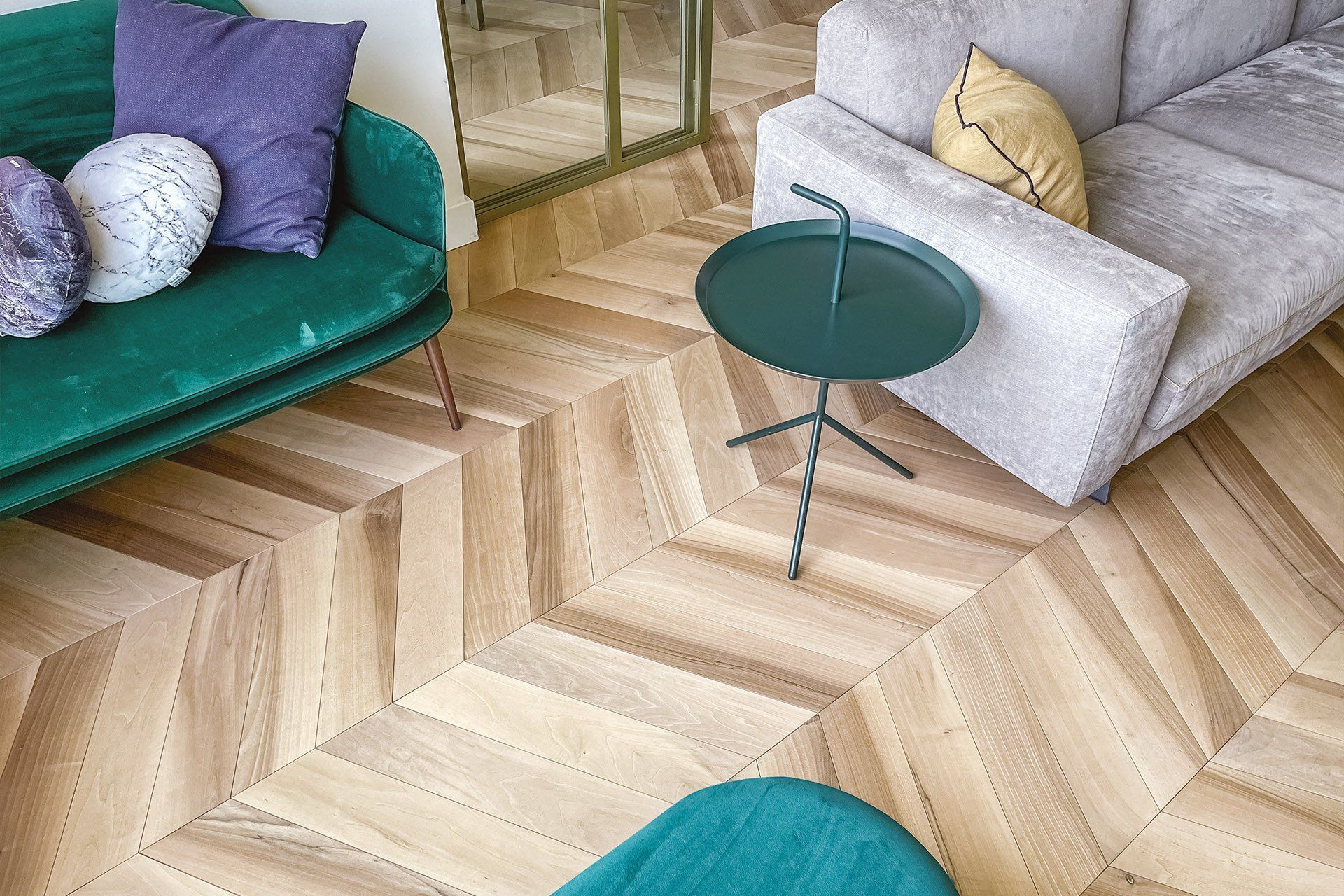 Soggiorno moderno con pavimento in legno a spina di pesce, divani grigi e verdi e un piccolo tavolino rotondo.