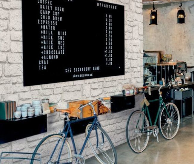 Biciclette parcheggiate accanto al bancone di un bar e a una lavagna nera con il menù su un muro di mattoni bianchi.