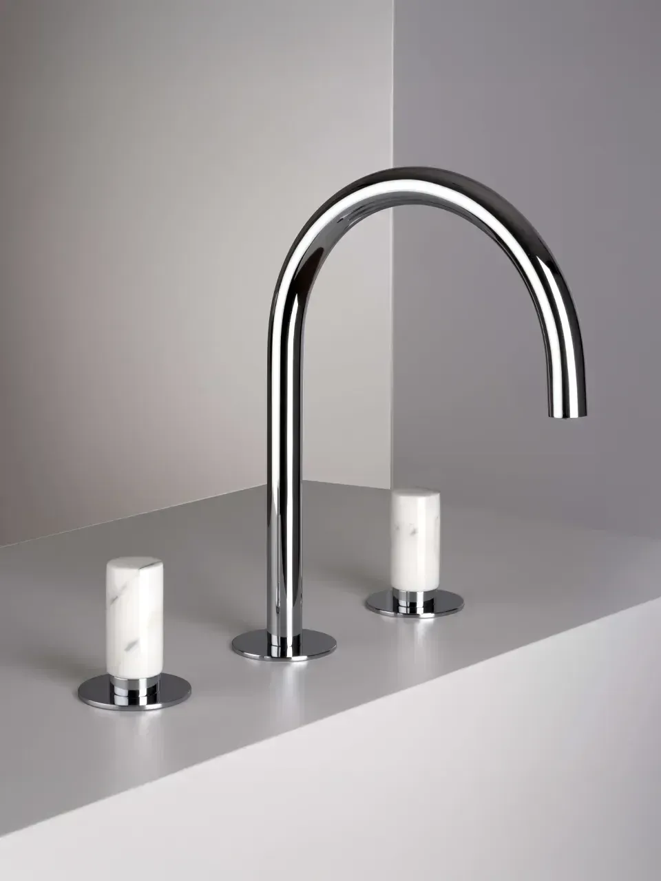 Rubinetto cromato con due maniglie bianche su un piano lavabo grigio.