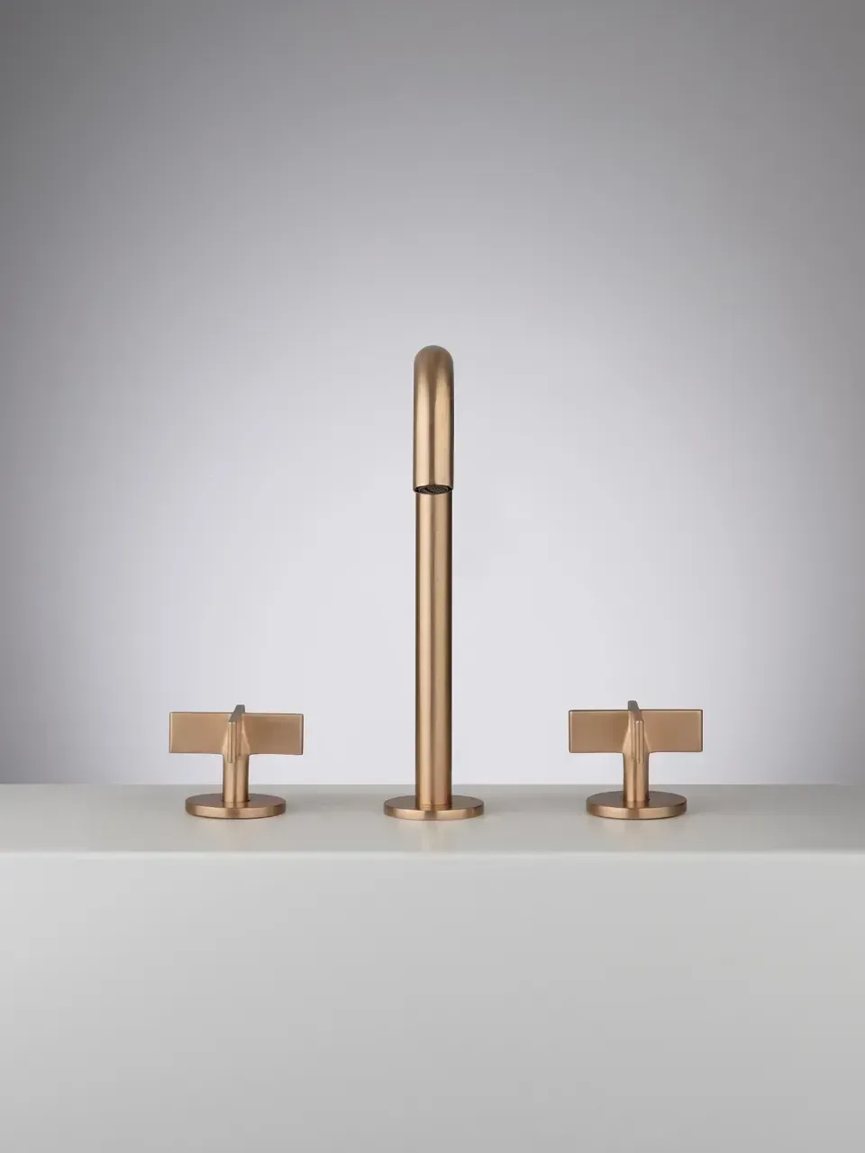 Lampada minimalista in ottone posizionata al centro tra due piccoli tavolini coordinati su uno sfondo grigio chiaro.