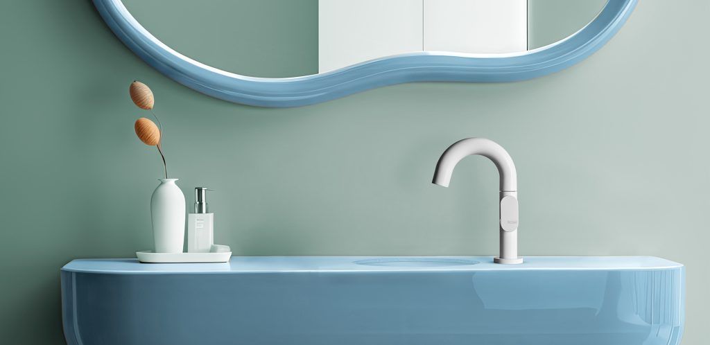 Lavabo da bagno moderno con mobile blu, specchio rotondo e rubinetto bianco su una parete verde salvia.