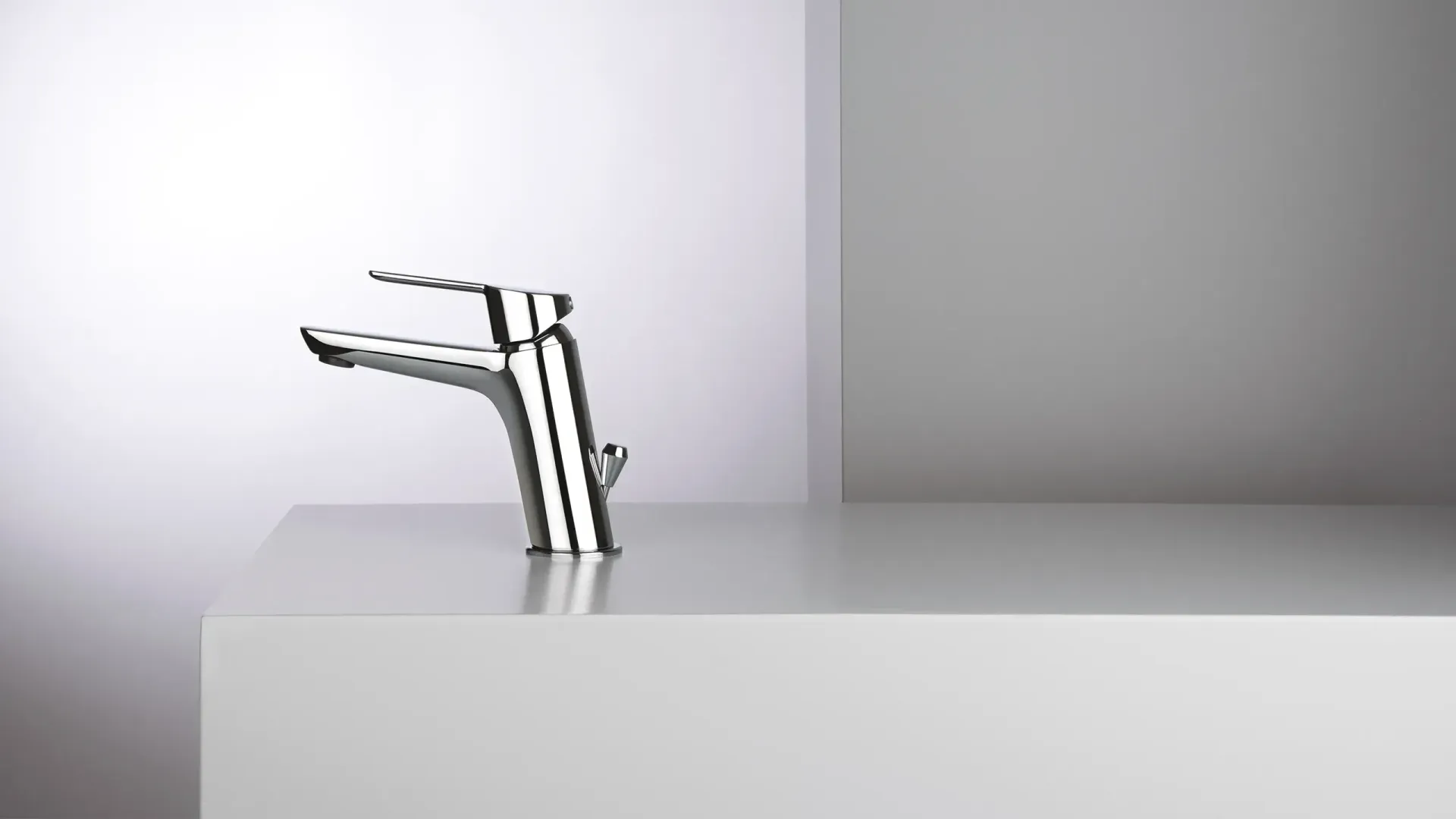 Rubinetti metallici che sporgono da un lavabo bianco su uno sfondo grigio minimalista.