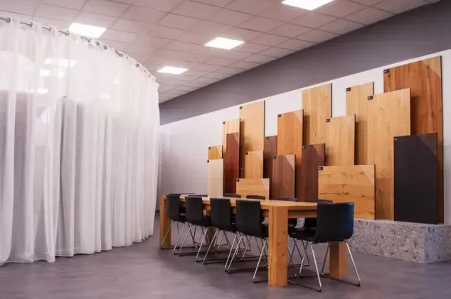Sala relax moderna per ufficio con parete divisoria in legno, lungo tavolo e sedie nere su pavimento grigio.