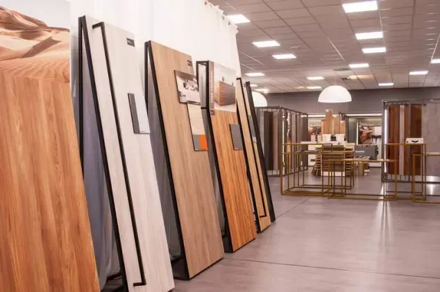 Interno di uno showroom di pavimenti con grandi campioni di legno e piastrelle esposti lungo la parete.