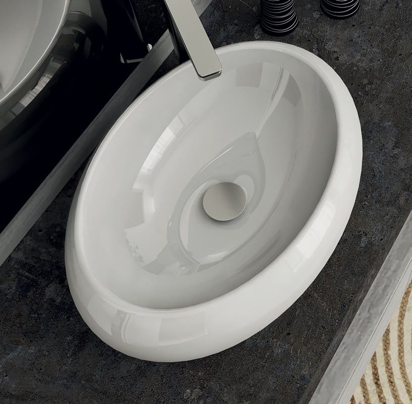 Lavabo rotondo bianco moderno da appoggio su un mobile bagno scuro accanto a un rubinetto