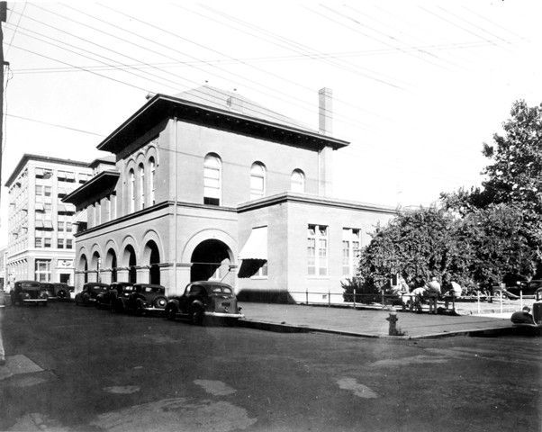A black and white photo of a large building with cars parked in front of it