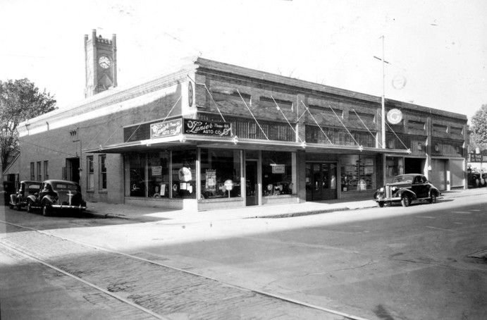 A black and white photo of a building with cars parked in front of it.