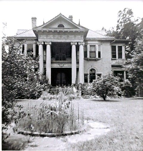 A black and white photo of a large house with columns