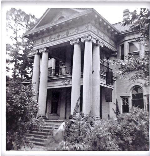A black and white photo of an old house with columns