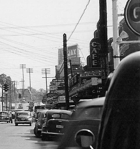 A black and white photo of a city street with a jax cafe sign