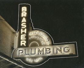 A neon sign for brasier plumbing is lit up at night