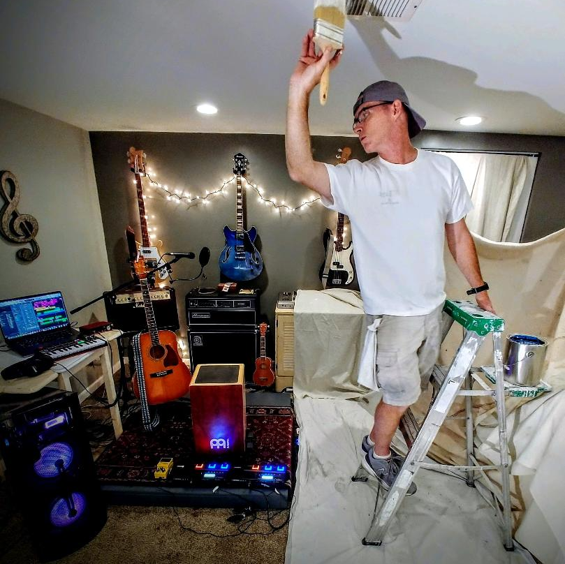 A man paints the ceiling of a room with guitars in the background