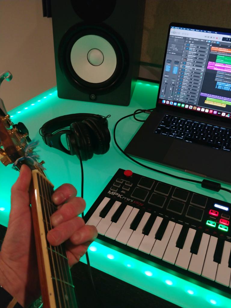 A person playing a guitar next to a keyboard and a laptop