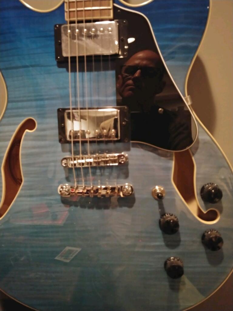 A blue guitar with a reflection of a man on it
