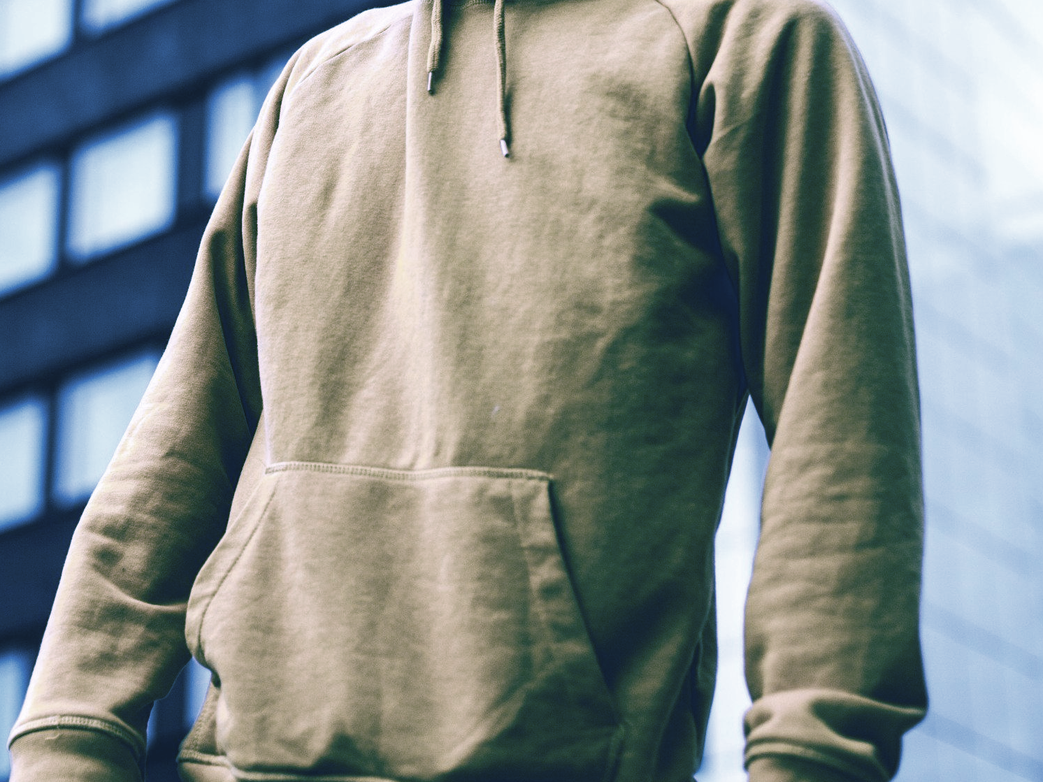 A man wearing a tan hoodie is standing in front of a building