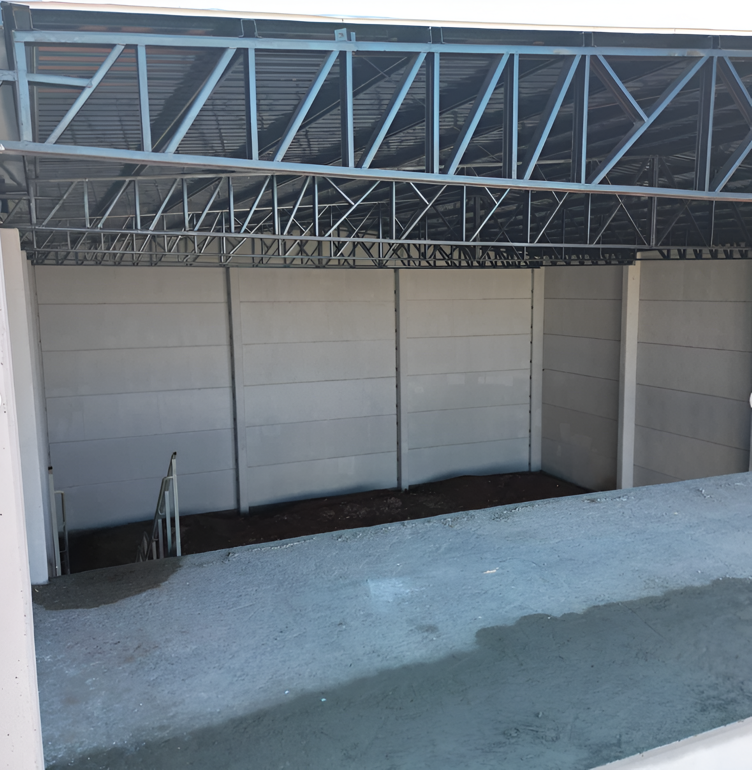 Área coberta, com a frente aberta, painéis modulares cinza-claro, telhado com estrutura metálica e uma escada à esquerda.