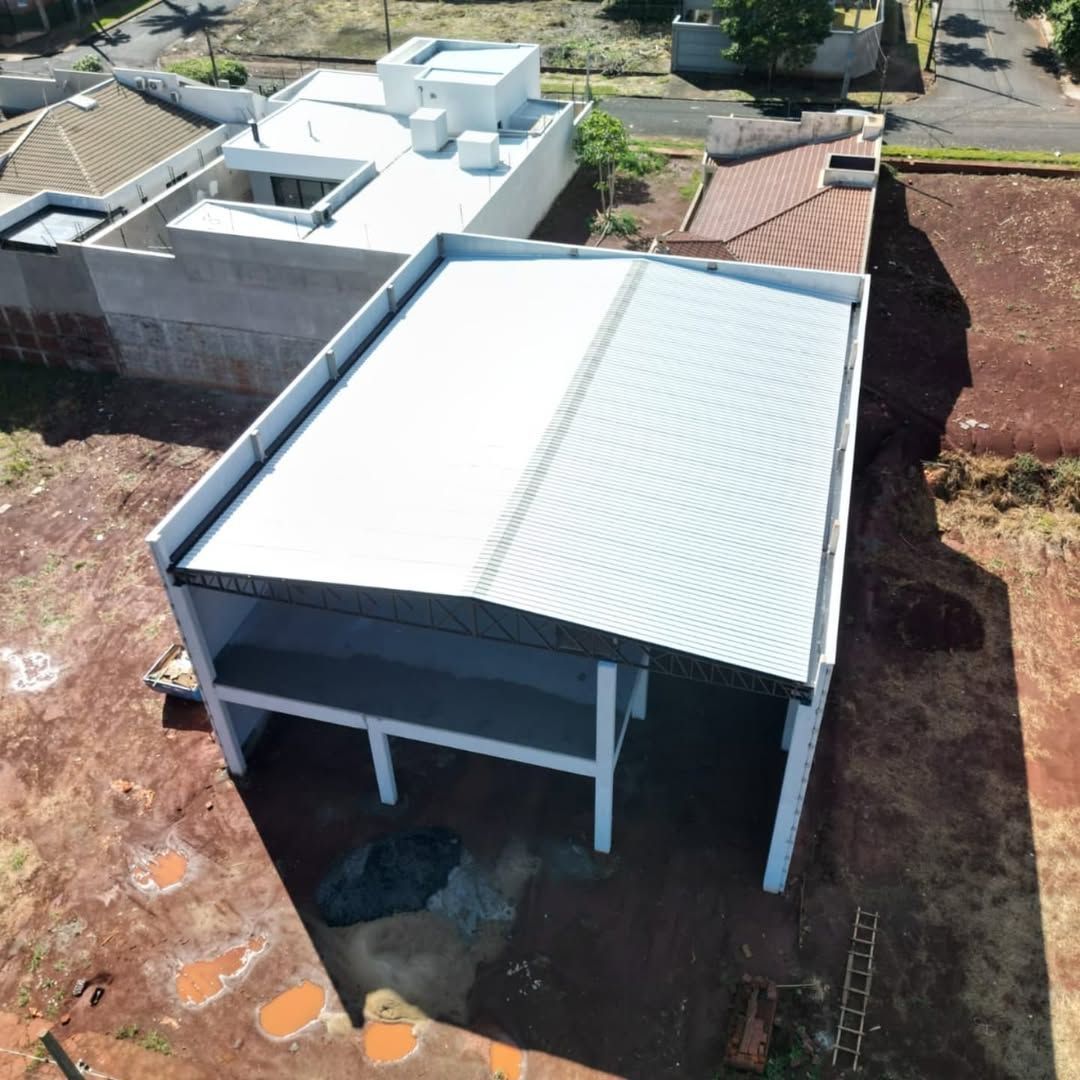 Vista aérea de uma obra retangular em construção, com telhado metálico e colunas de concreto aparente sobre o solo.
