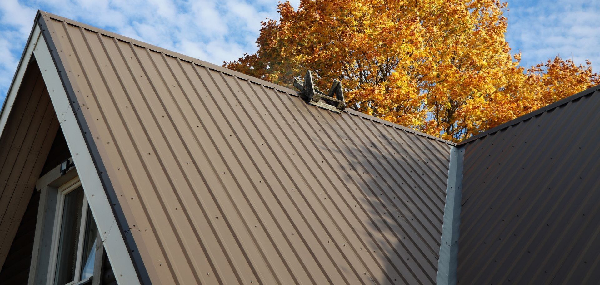 Toit en métal marron d'un bâtiment avec un ciel bleu et un feuillage d'automne en arrière-plan.