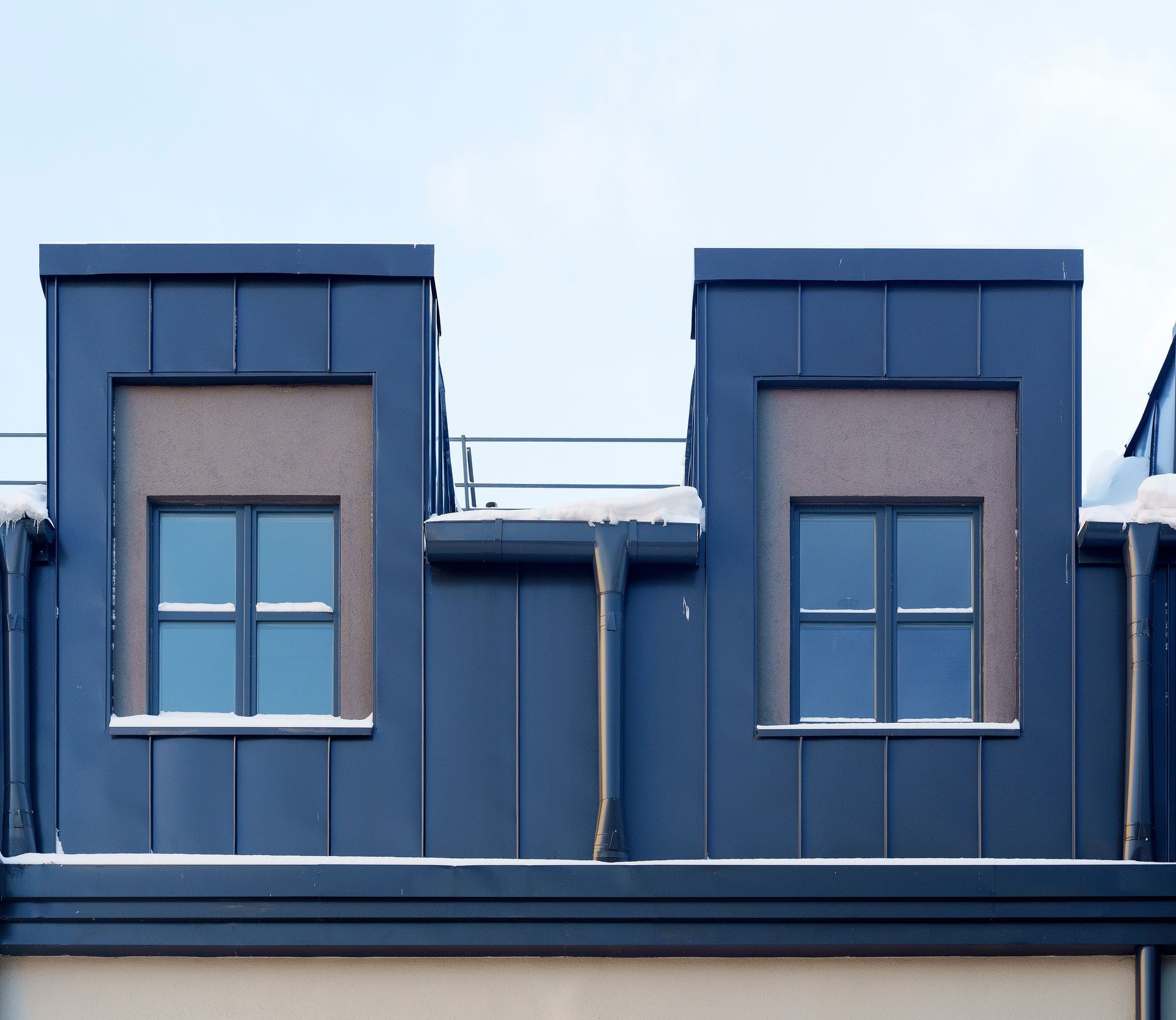 Deux lucarnes rectangulaires bleues avec des fenêtres placées dans des panneaux texturés marron sur un bâtiment contre un ciel clair.