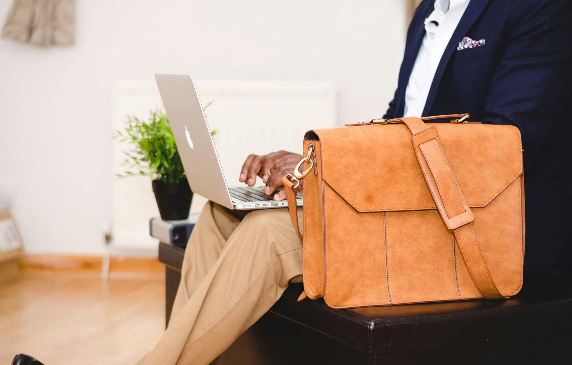 Man in suit working on laptop, brown briefcase on a stool.
