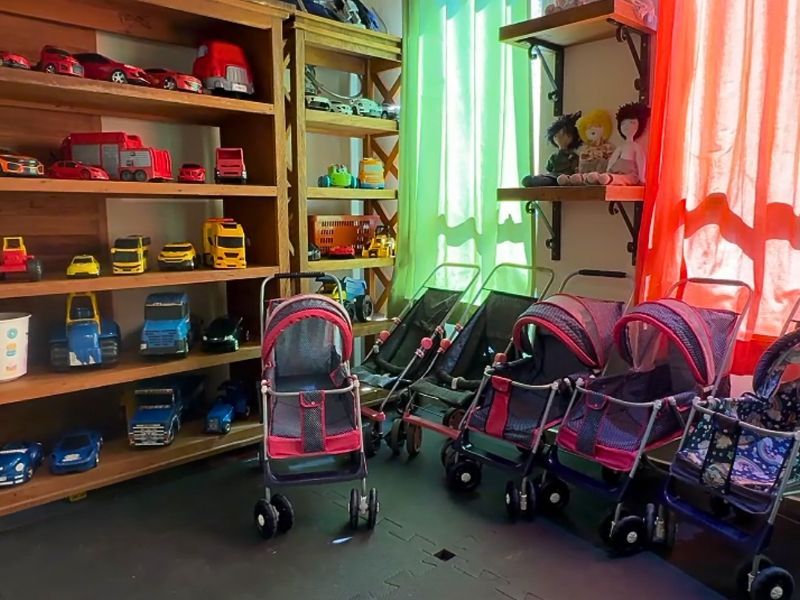 Prateleiras com carrinhos de brinquedo, carrinhos de bebê e cortinas coloridas.