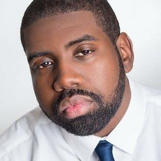 A man with a beard is wearing a white shirt and blue tie.