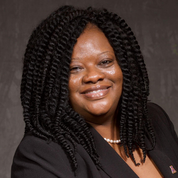 A woman with braids and a pearl necklace smiles for the camera