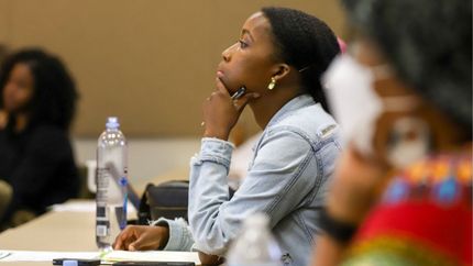 A woman is sitting at a table with her hand on her chin.