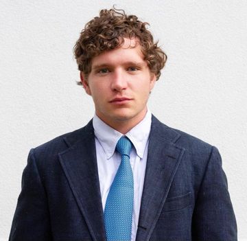 A man with curly hair is wearing a suit and tie