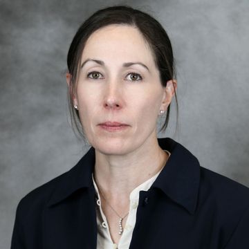 A woman in a blue jacket and white shirt is looking at the camera.