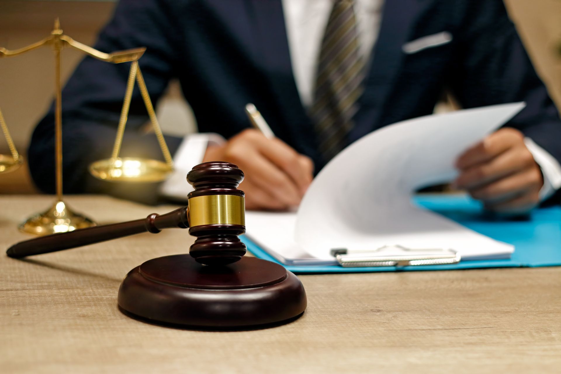 A Man in a Suit is Writing on a Piece of Paper Next to a Judge 's Gavel — Perth, WA — Lenhoff & Hotz