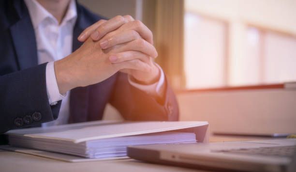 A Man in a Suit is Sitting at a Desk with his Hands Folded — Perth, WA — Lenhoff & Hotz