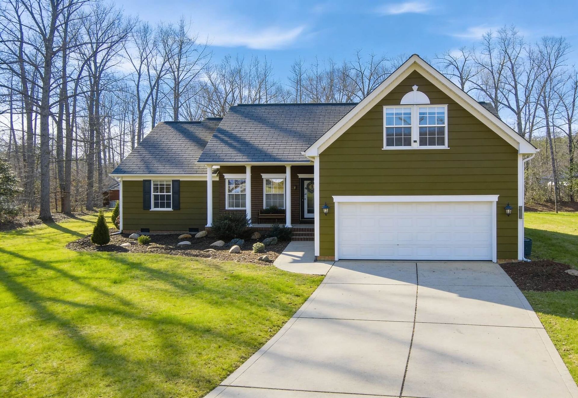Green house with a white garage door and a concrete driveway on a sunny day.