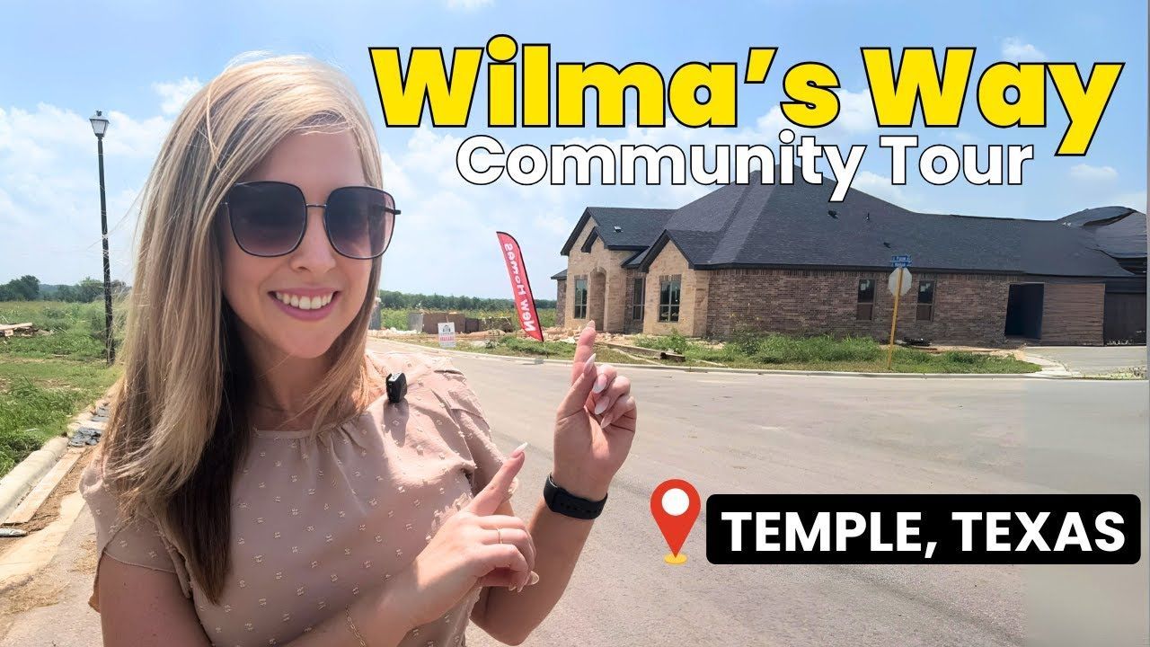 A woman wearing sunglasses is giving a thumbs up in front of a house.