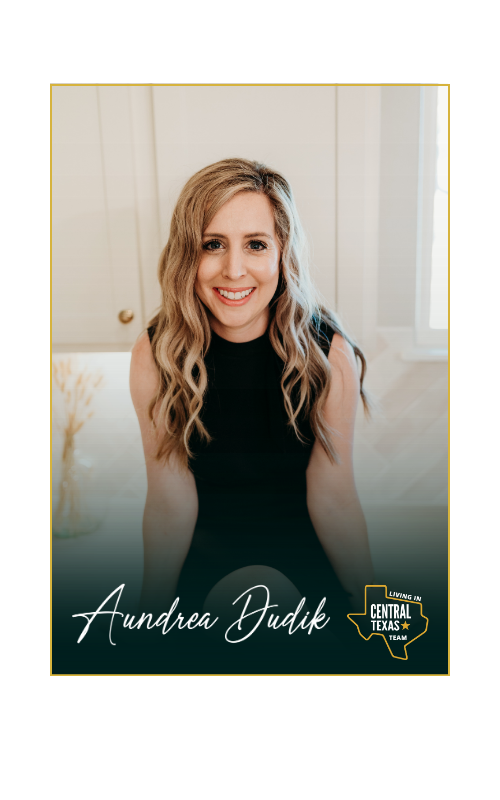A woman in a black dress is sitting in front of a window and smiling.