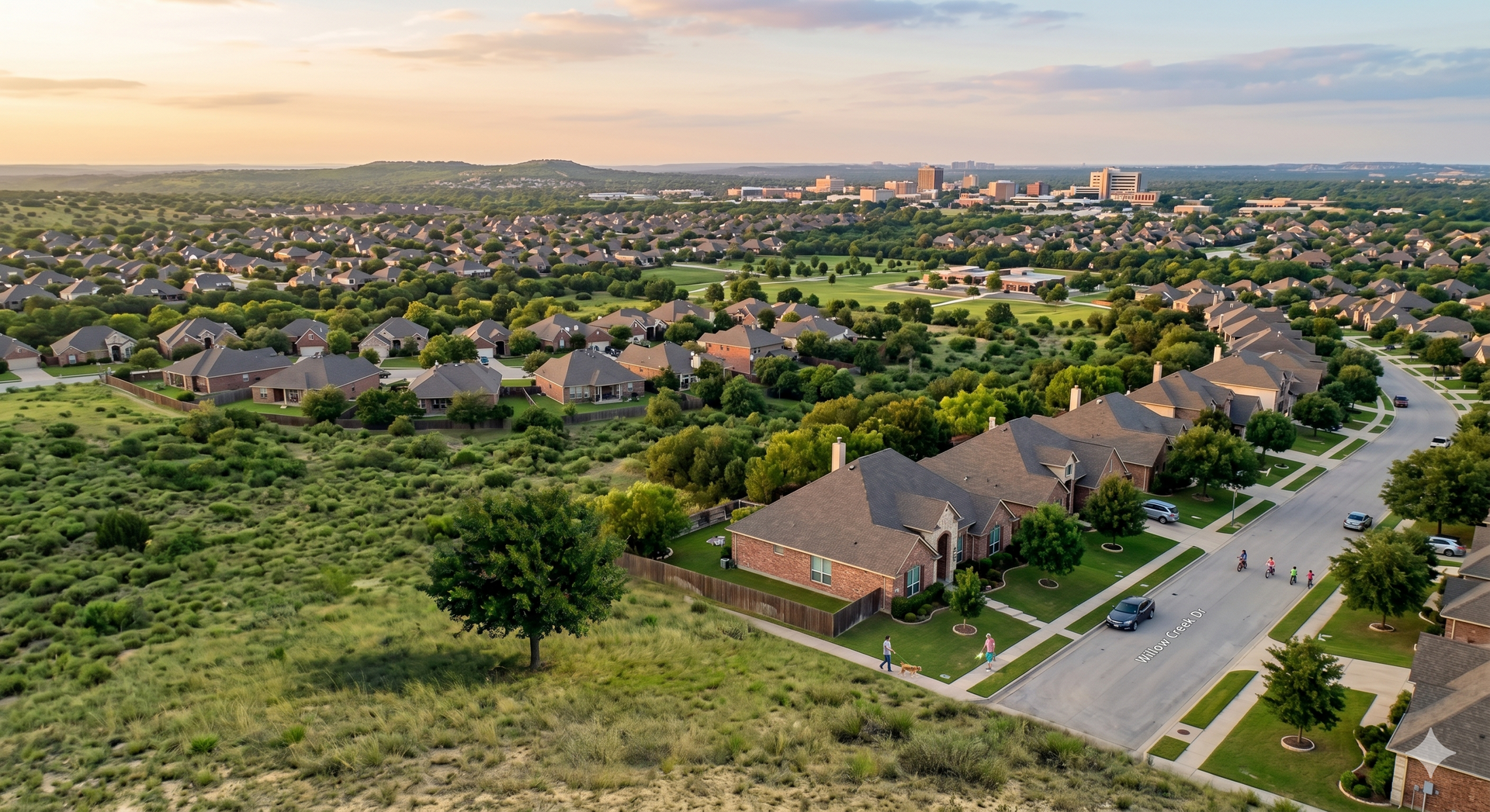 Aerial view of a suburban neighborhood with rows of houses, green fields, and roads at sunset